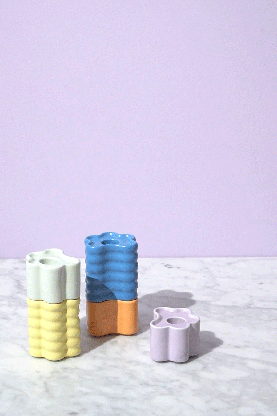 Three Octaevo Flora Candle Holders with wavy edges sit on marble, set against a wall.