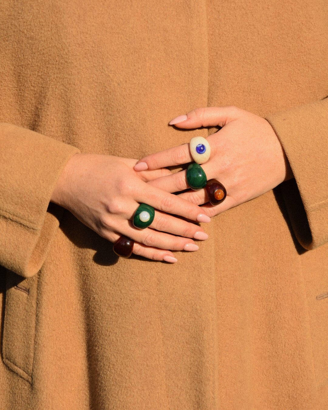 Close-up of hands wearing multiple rings with a brown coat background