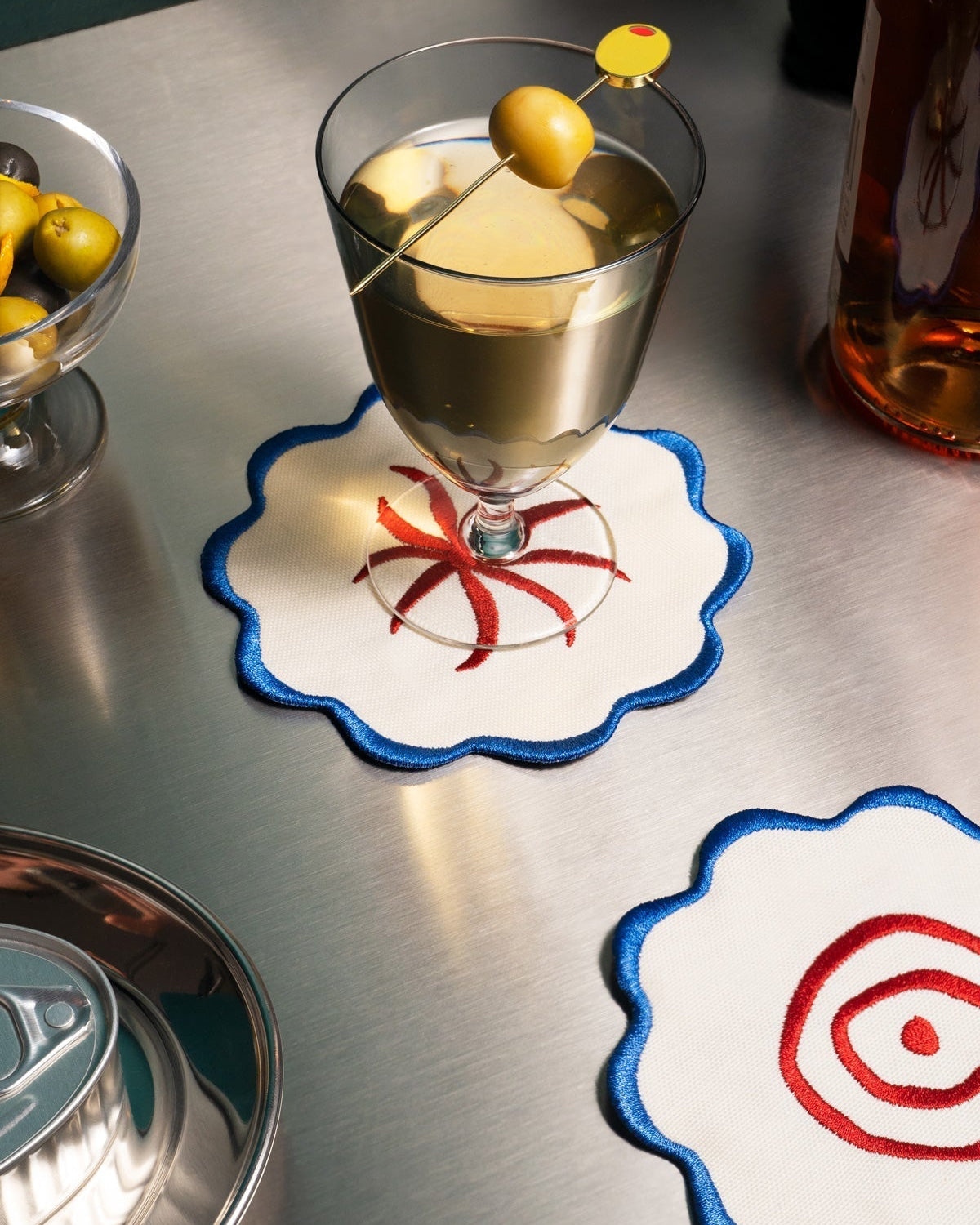A martini with an olive sits on Octaevo Amalfi Coasters beside olives, a canned drink, and another coaster.
