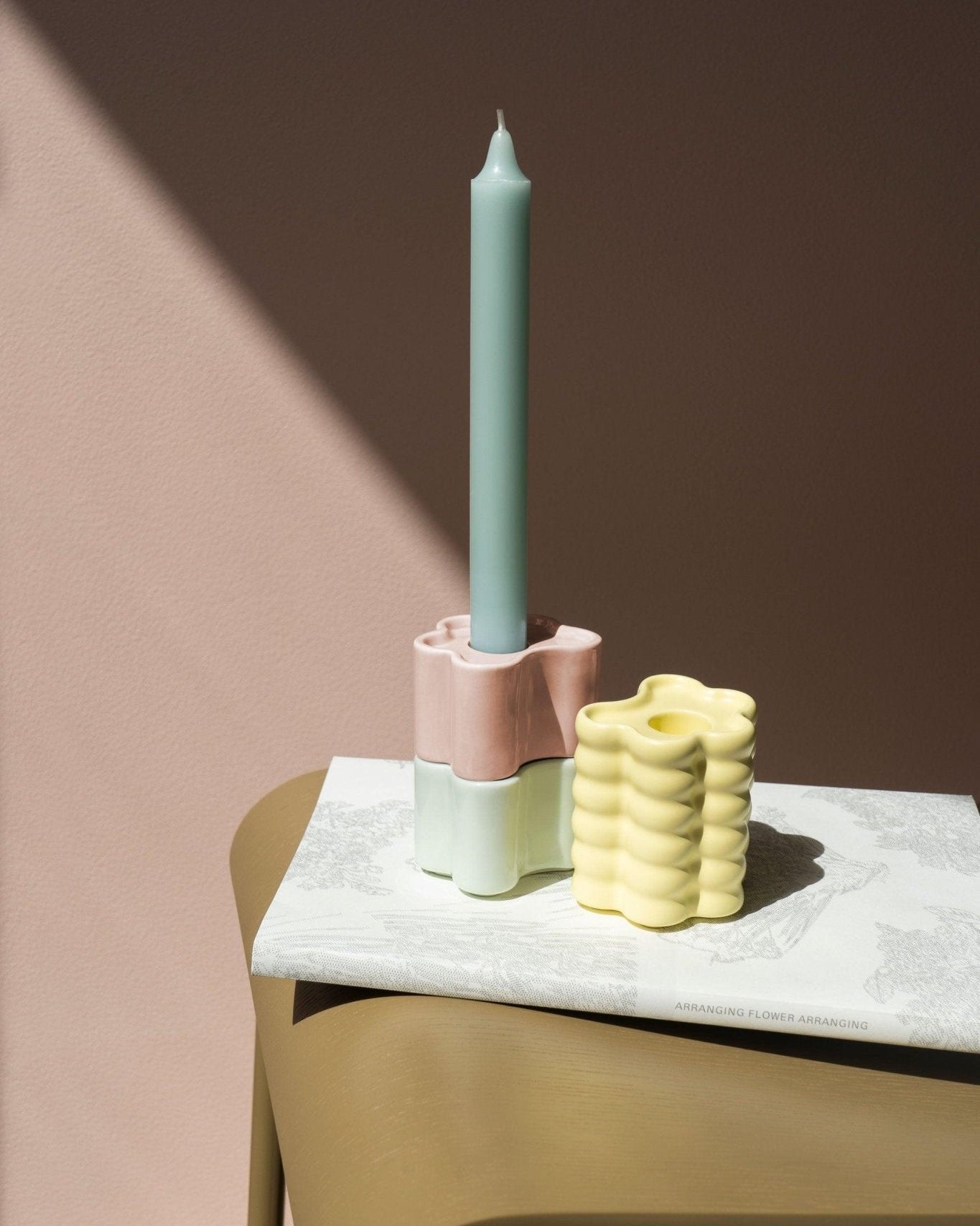 The Octaevo Flora Candle Holder in hand-glazed in mint with a pastel blue candle sits beside a small yellow vase.