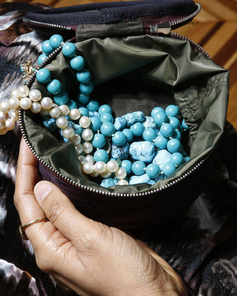 Hand holding a bag with turquoise and pearl necklaces