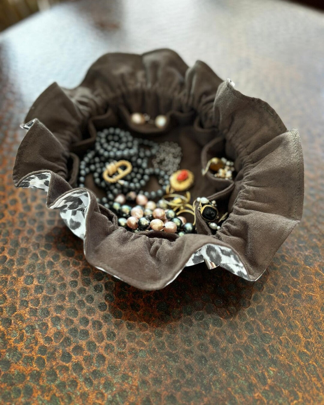 Brown fabric jewelry organizer with jewelry on a textured surface