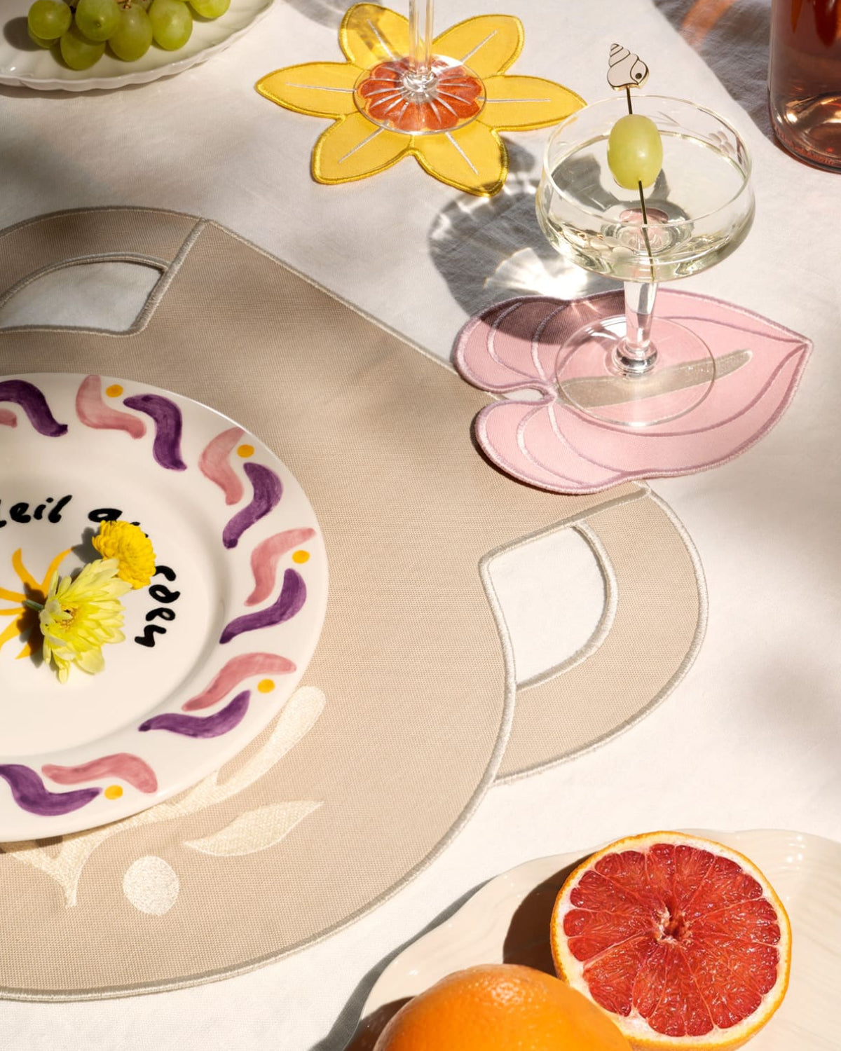 A table setting with fruit, cocktails, and Octaevo Pink Anthurium Coasters (Set of 4) on a white floral cloth.