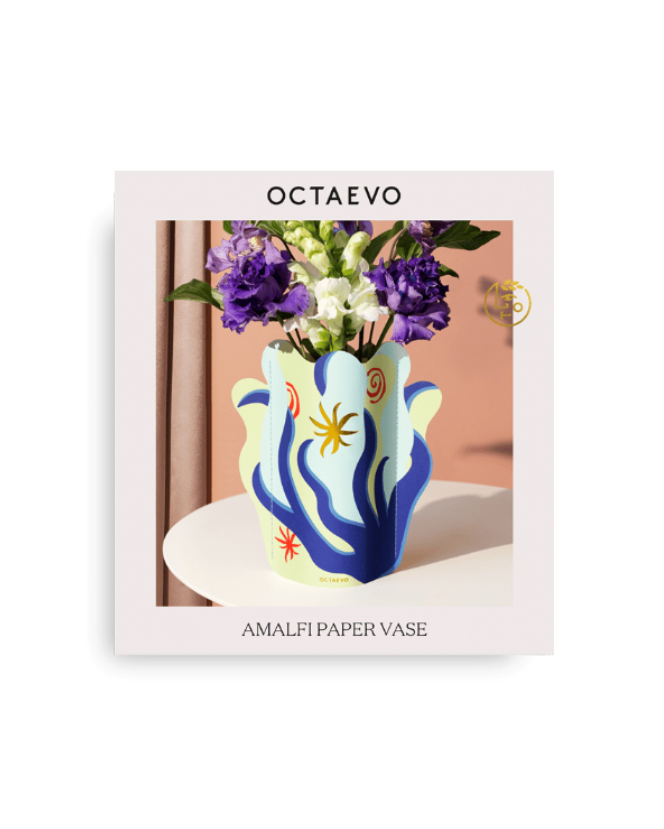 The Octaevo Amalfi Mini Paper Vase, with purple and white flowers, stands on a white table.