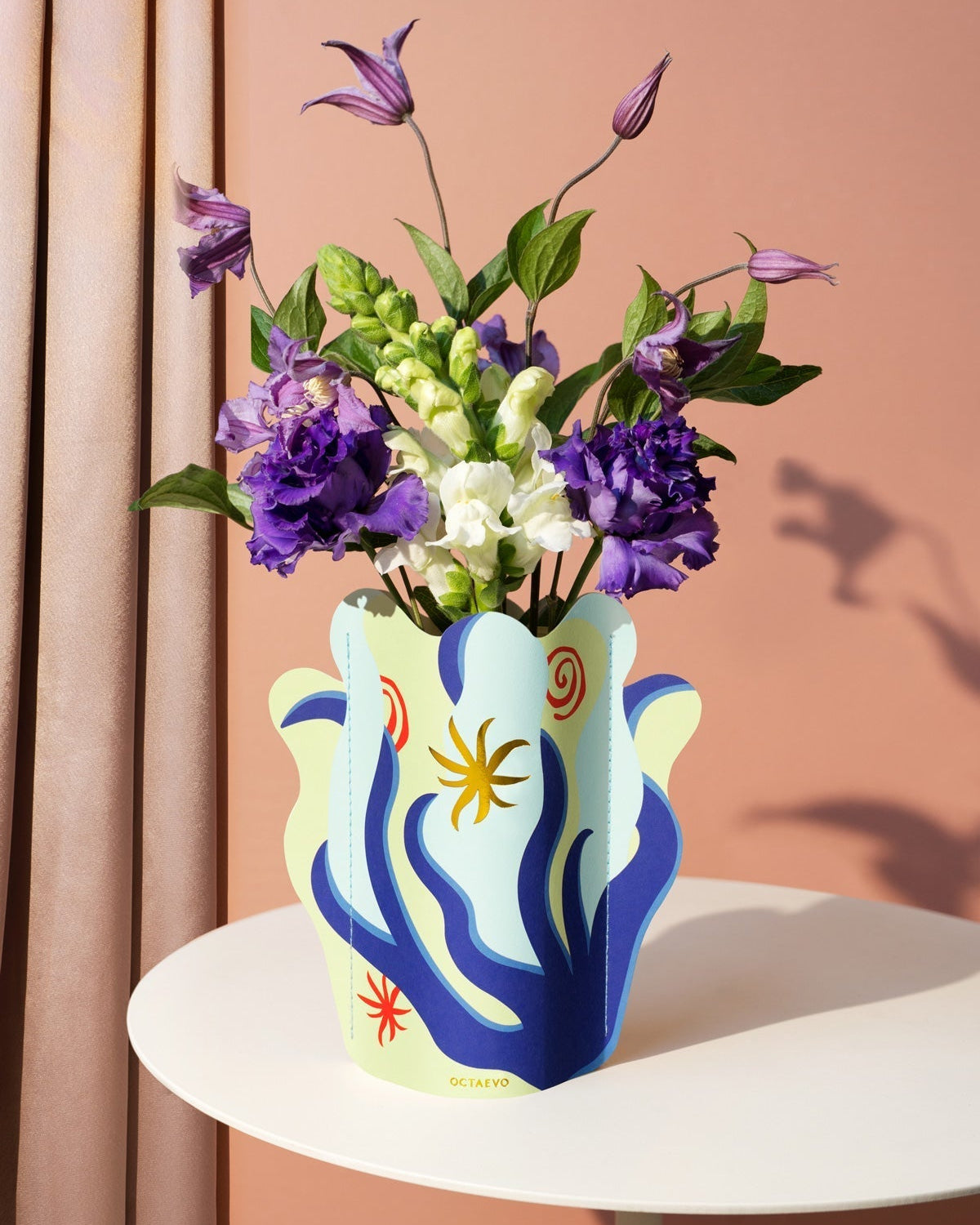 The Amalfi Mini Paper Vase by Octaevo features abstract patterns and brightens tables with Mediterranean coral vibes.