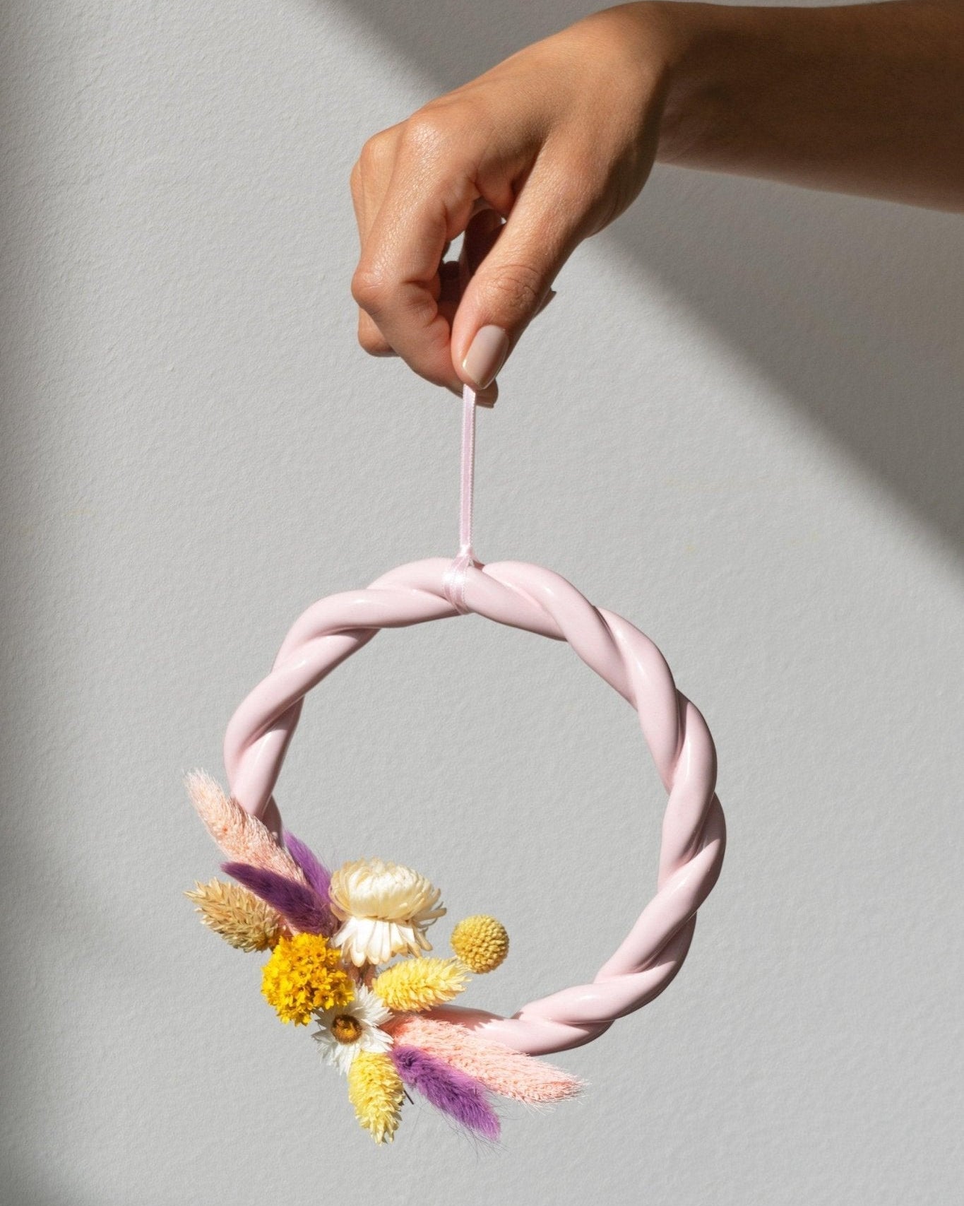 A hand holds the pink OCTAEVO Sicilia Ceramic Trivet, perfect as earthenware wall decor against a light gray background.