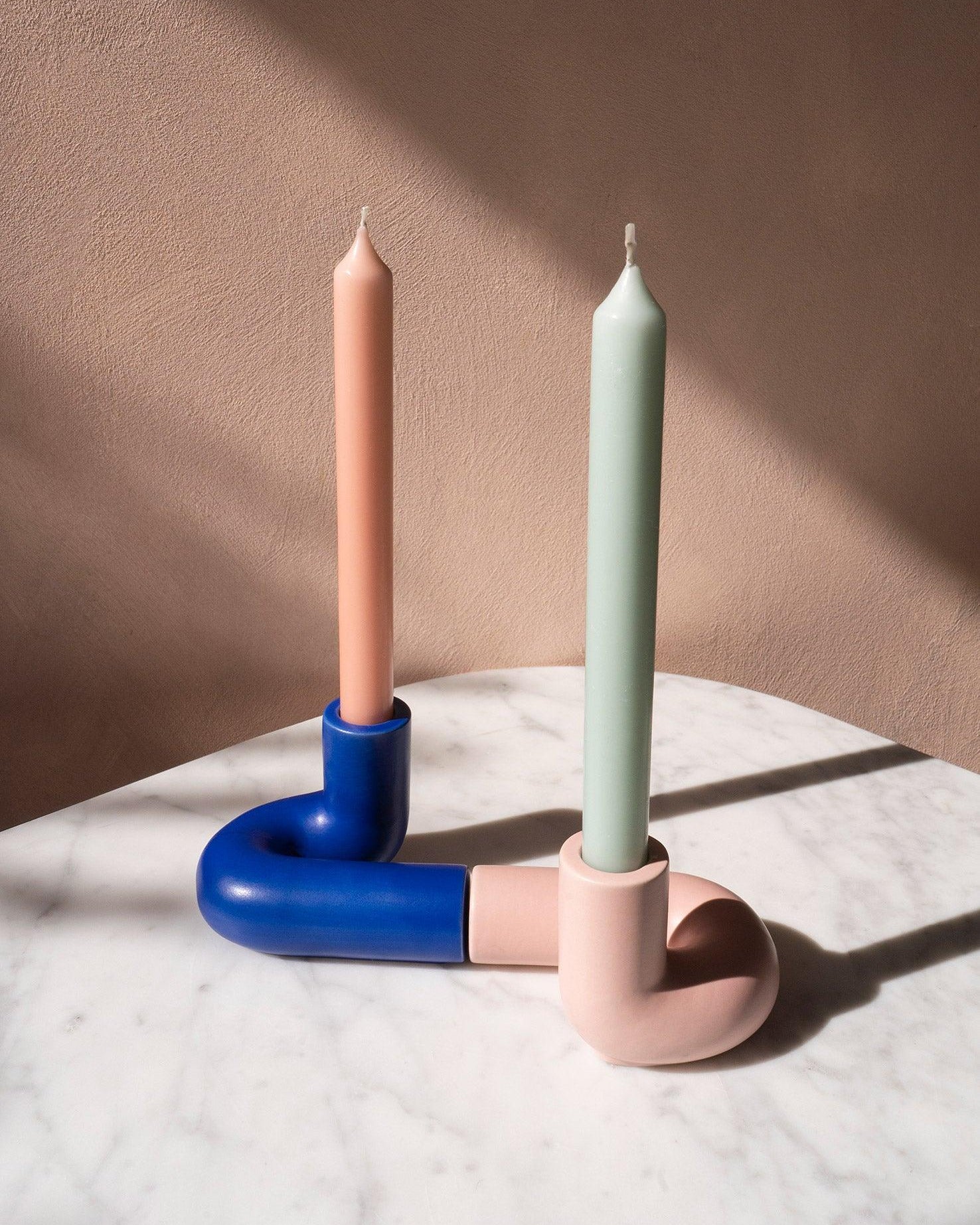 Two pastel candles in blue OCTAEVO Templo Candle Holder on white marble, set against a beige wall.