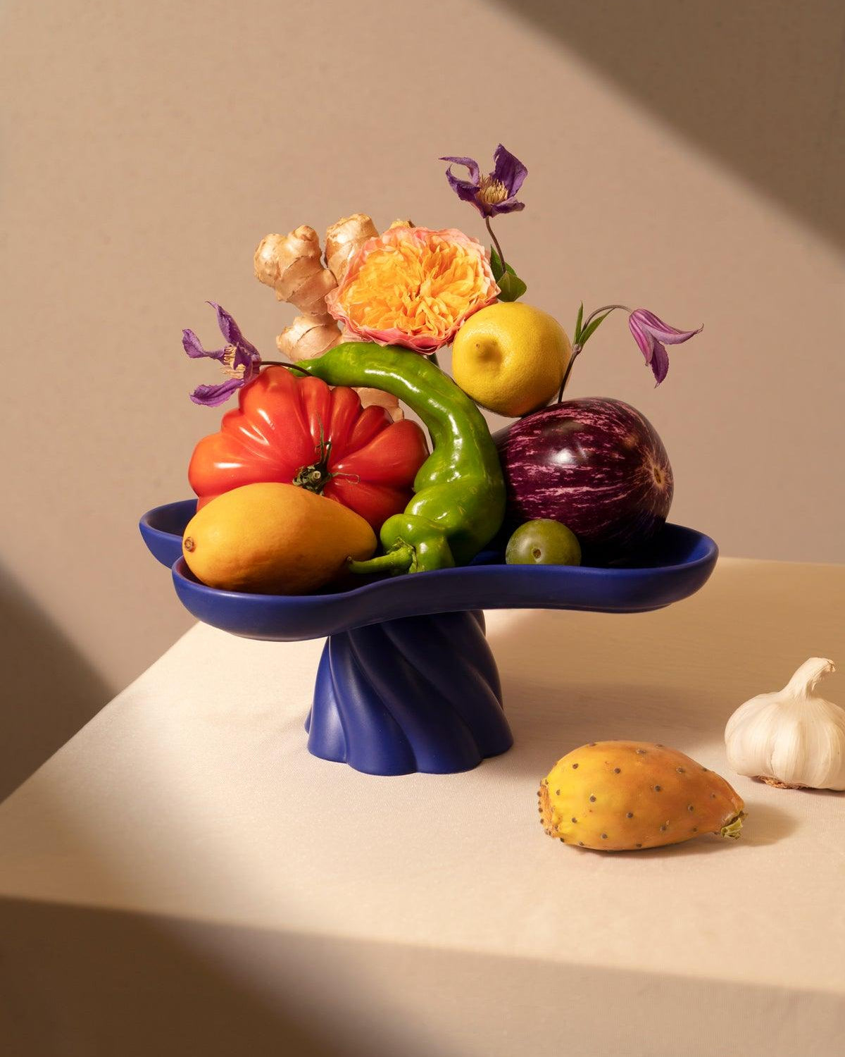 Colorful fruits and veggies on the Octaevo Templo High Tray in blue, with garlic and prickly pear beside the blue centerpiece