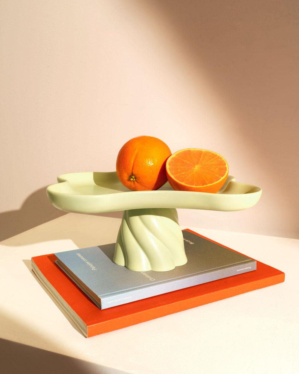 A light mint Octaevo Templo High Tray holds oranges and sits on books against a warm, minimal backdrop.