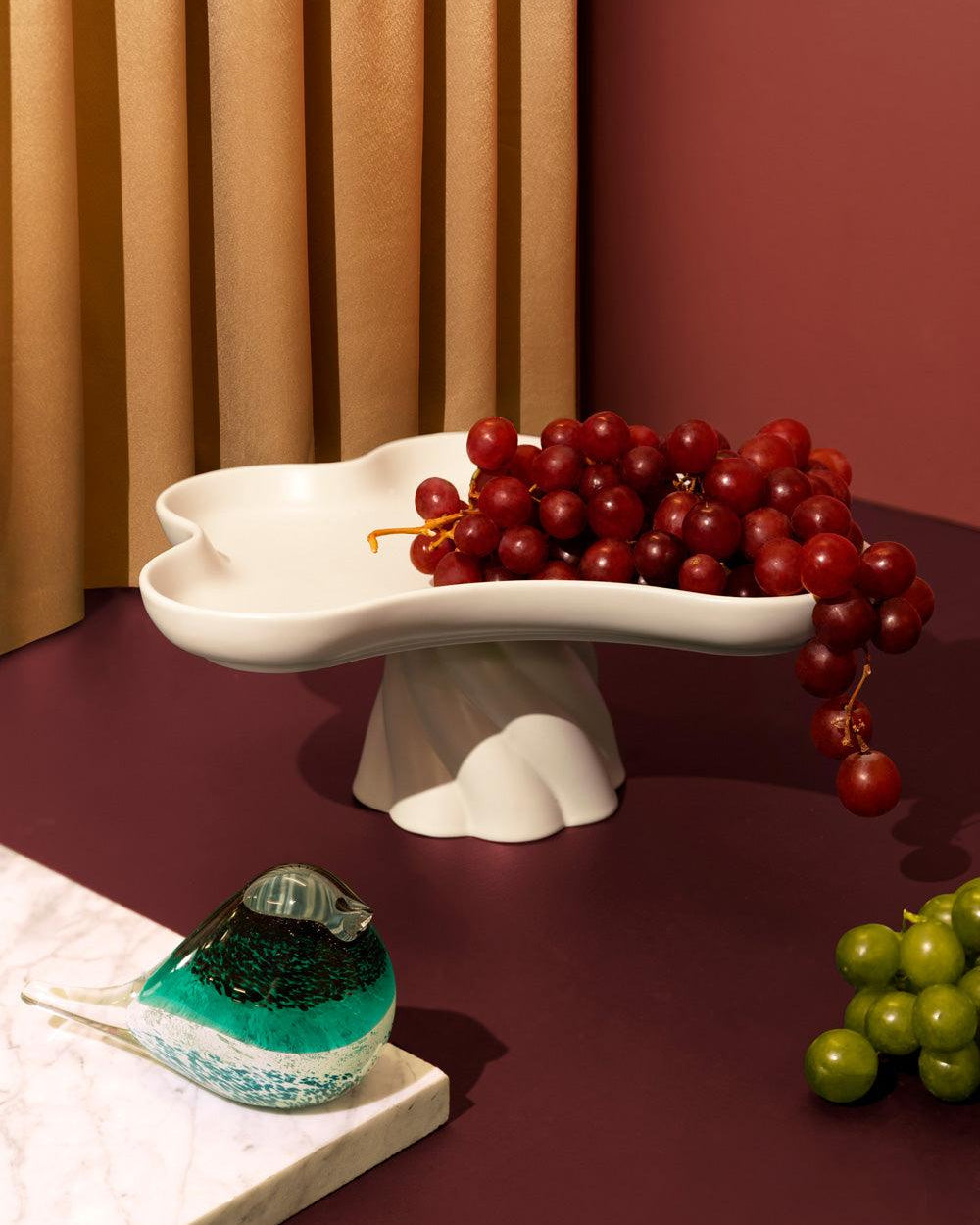 Red grapes on Octaevo’s ivory, flower-shaped Templo High Tray make a striking centerpiece with glass and green grapes.